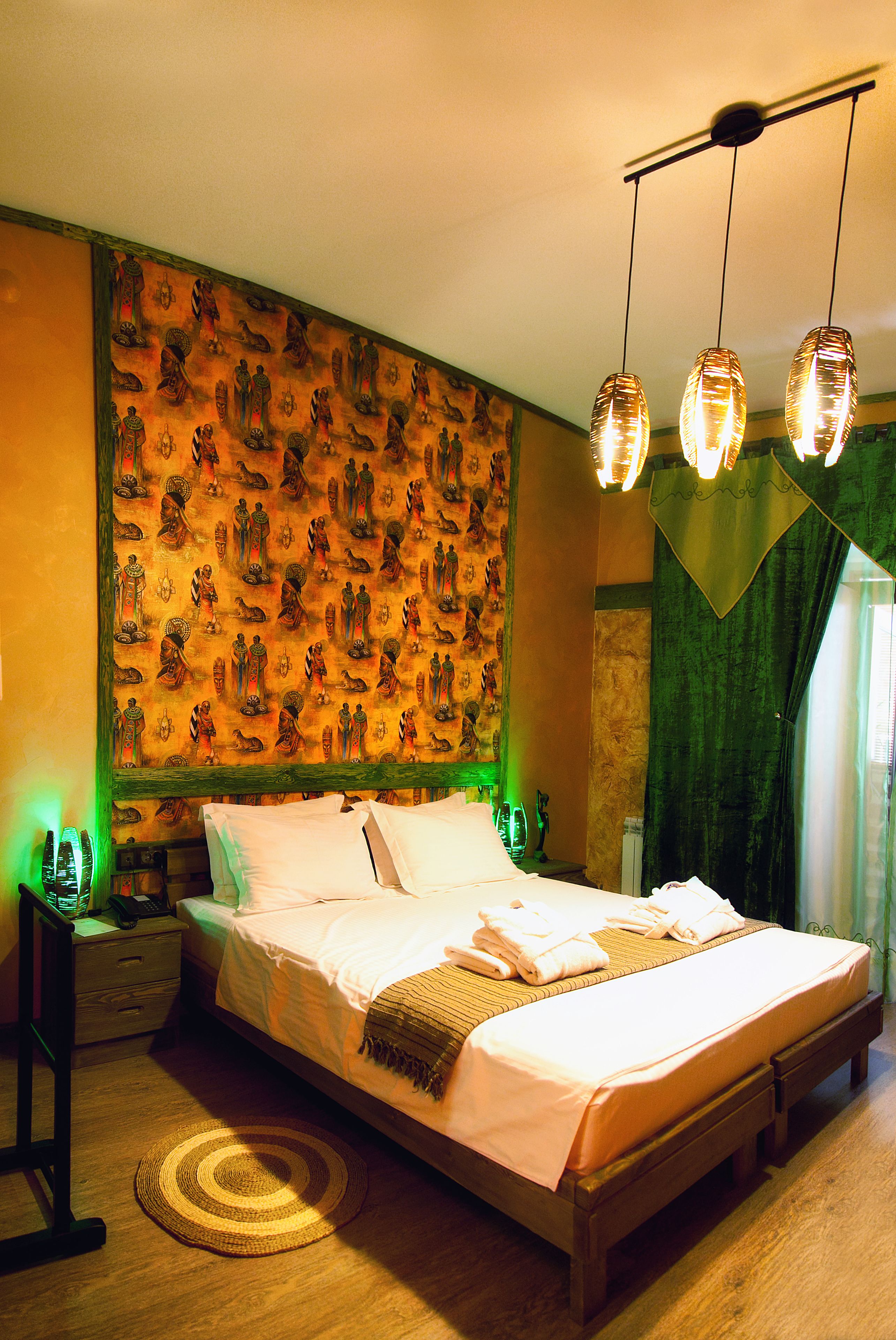 A hotel room with a large bed, a headboard with artwork, a bedside table with a lamp, and a window with curtains.