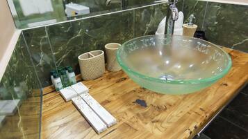 A bathroom with a large glass bowl sink, wooden countertop, and toiletries.