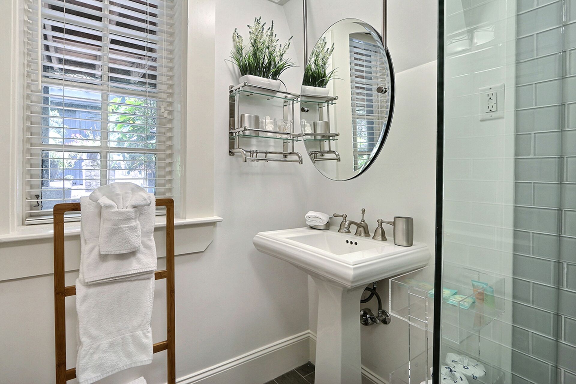 A bathroom with a white sink, a glass shower enclosure, and a wooden towel rack.