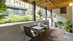 An outdoor patio with a brick floor, two metal chairs, a table with a bowl of fruit, and potted plants. - Heated Pool Access | 5*Clean | Flex Cancelation (Savannah)