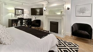 Quarto com cama grande, lareira, televisão e escrivaninha com abajur.