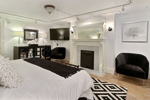 A bedroom with a large bed, a fireplace, a TV, and a desk with a lamp. - Heated Pool Access | 5*Clean | Flex Cancelation (Savannah)