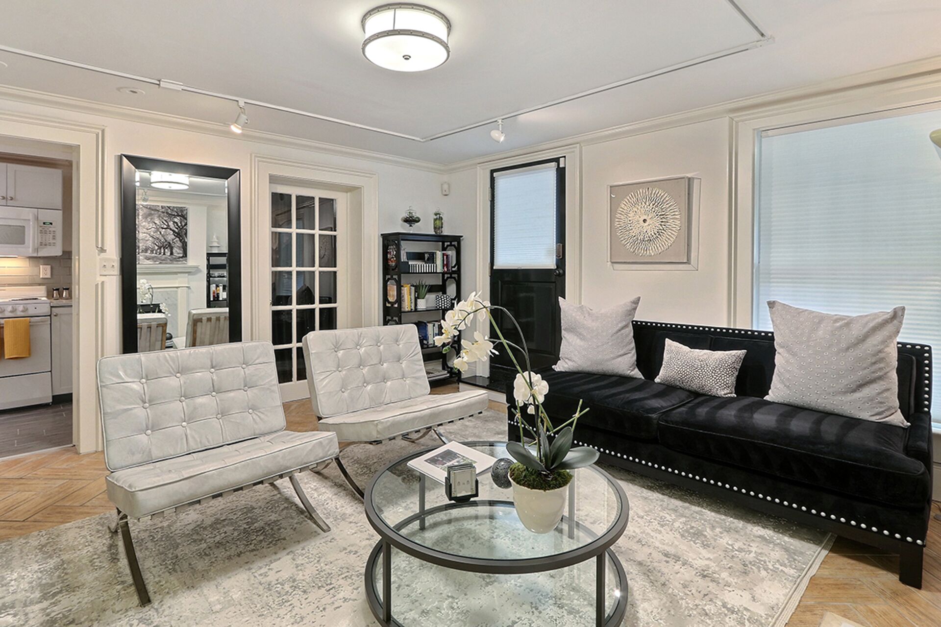 Ein Wohnzimmer mit schwarzem Sofa, weißen Sesseln, einem Glastisch und einem Bücherregal.
