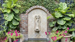 A stone fountain with a fish sculpture, surrounded by large potted plants and flowering shrubs. - Heated Pool Access | 5*Clean | Flex Cancelation (Savannah)
