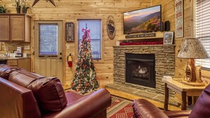 A cozy cabin interior with a stone fireplace, a Christmas tree, leather furniture, and a star on the ceiling. - Pigeon Forge River Front Cabin- Fishing Year Round-firepit with seating and Hottub (Pigeon Forge)
