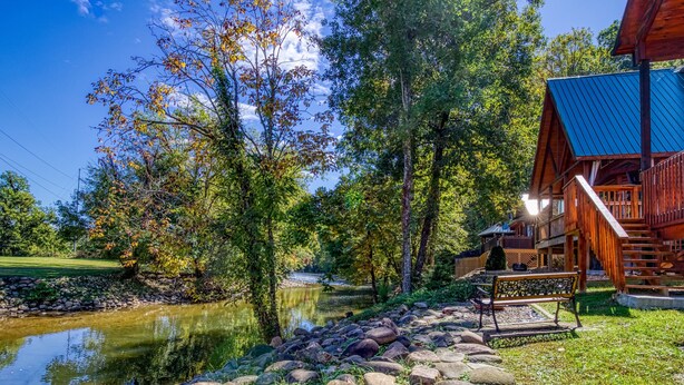 A wooden cabin with a stone pathway leading to a bench by a pond. - Pigeon Forge River Front Cabin- Fishing Year Round-firepit with seating and Hottub (Pigeon Forge)