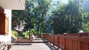 Eine Holzterrasse mit Picknicktisch und Stühlen, umgeben von einem Holenzaun und Bäumen.