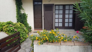 A building with a brown door and windows, a wooden bench, and yellow flowers in front. - Very bright villa standing 5 minutes walk from the beach  (Le Grau-du-Roi)