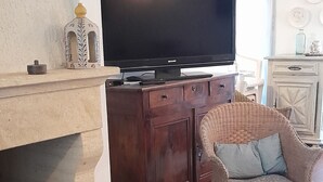 A living room with a fireplace, a television, a wicker chair, and a coffee table with magazines. - Very bright villa standing 5 minutes walk from the beach  (Le Grau-du-Roi)