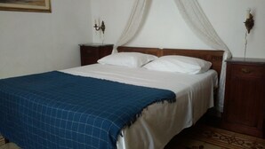 Un dormitorio con una cama, una manta azul, almohadas blancas, cabecera de madera, dos mesitas de noche y una lámpara fijada a la pared.