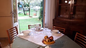 Comedor con una mesa dispuesta para cuatro, un frutero y vistas de un jardín a través de una puerta abierta.