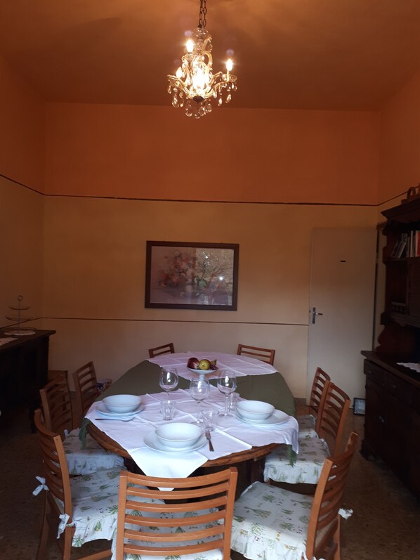 A dining area with a table set for four, surrounded by wooden chairs. A chandelier hangs from the ceiling, and a framed picture is on the wall.