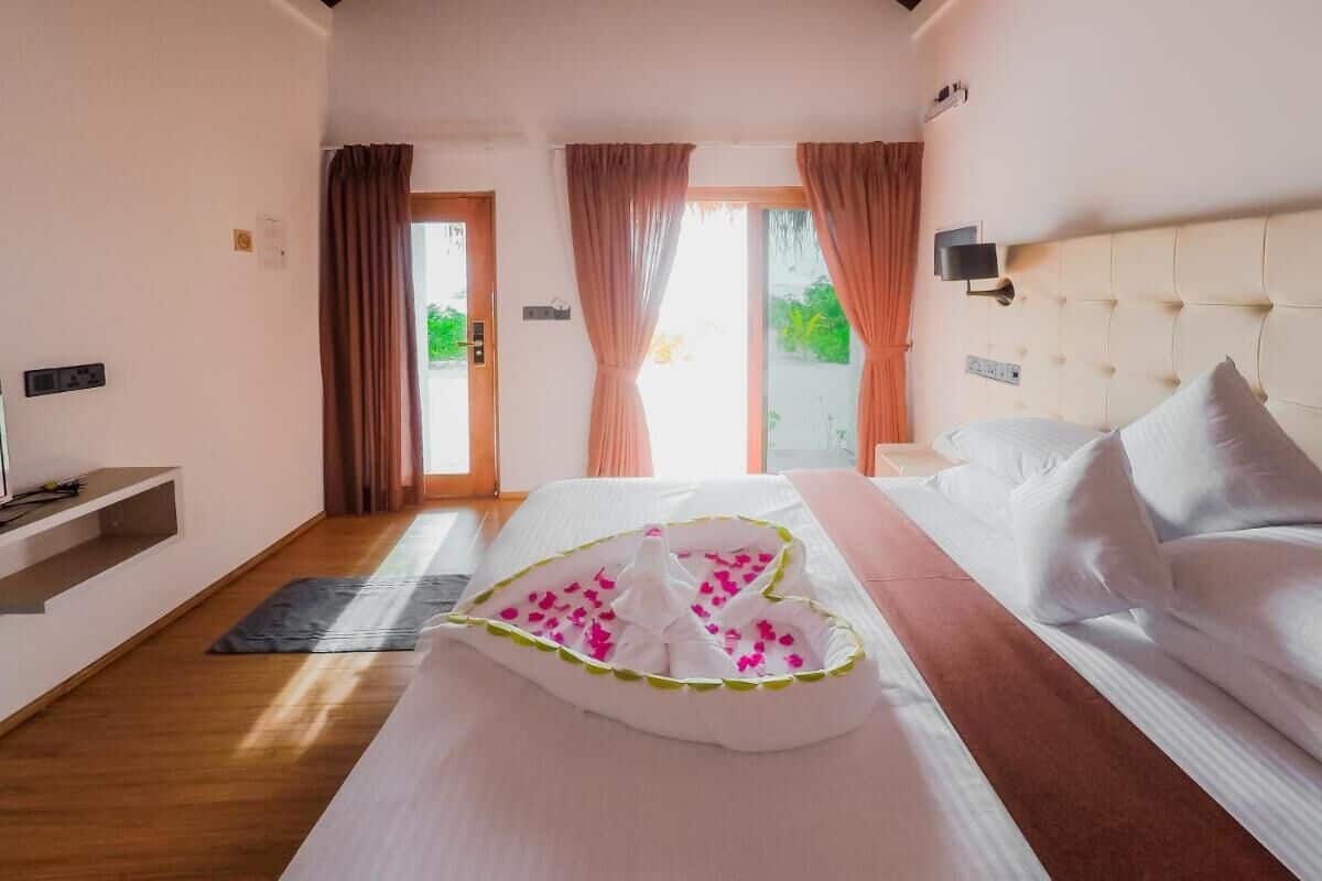 Una habitación de hotel con cama, mesita de noche, ventana con cortinas y vista a zonas verdes.