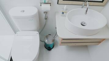 A modern bathroom with a toilet, bidet, sink, and hand wash dispenser.