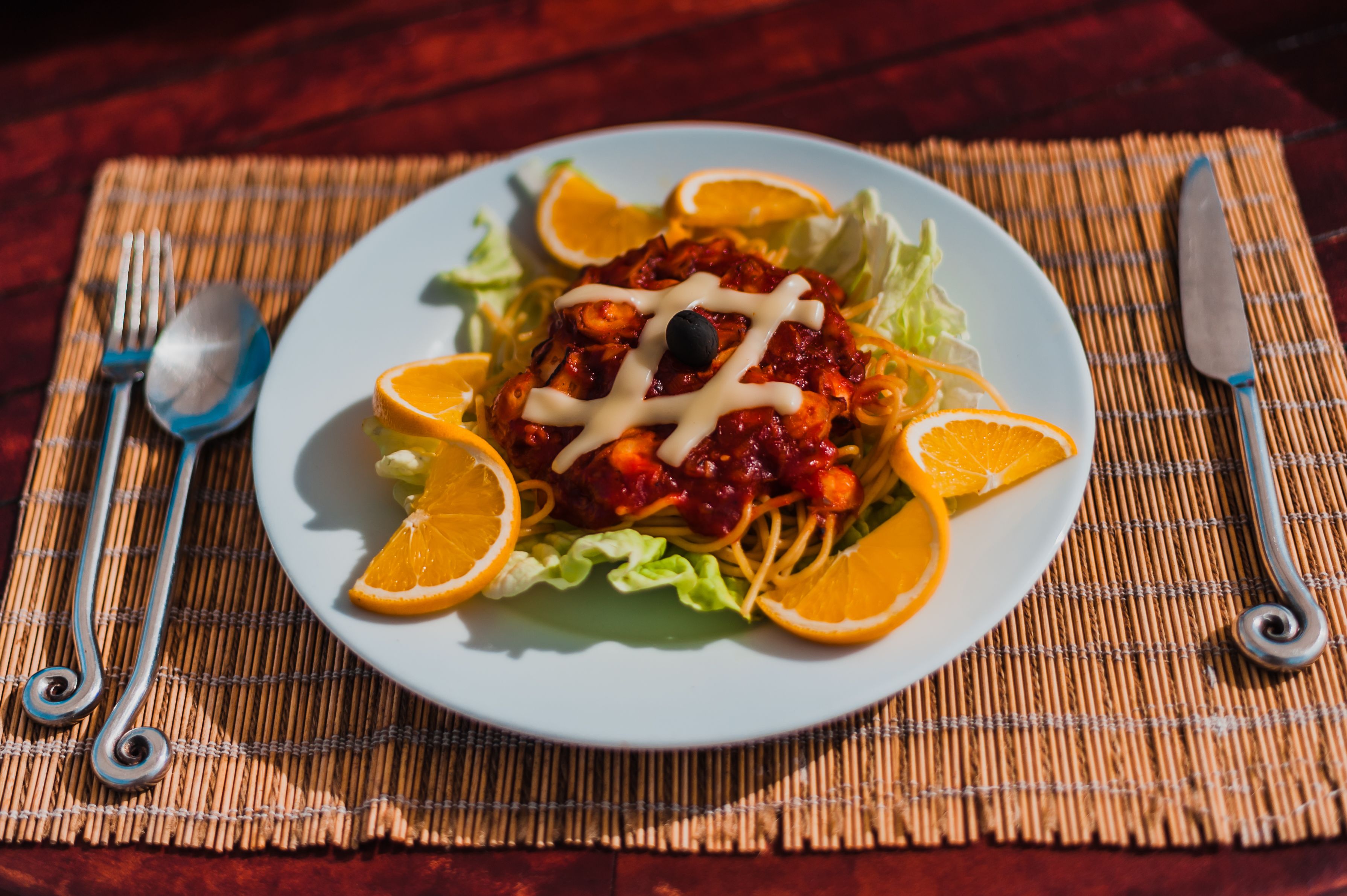 A plate of food with a red sauce, garnished with orange slices and a black olive, placed on a white plate with a green salad underneath.