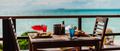 A wooden table with a view of the ocean, a bottle, and a glass of blue drink.