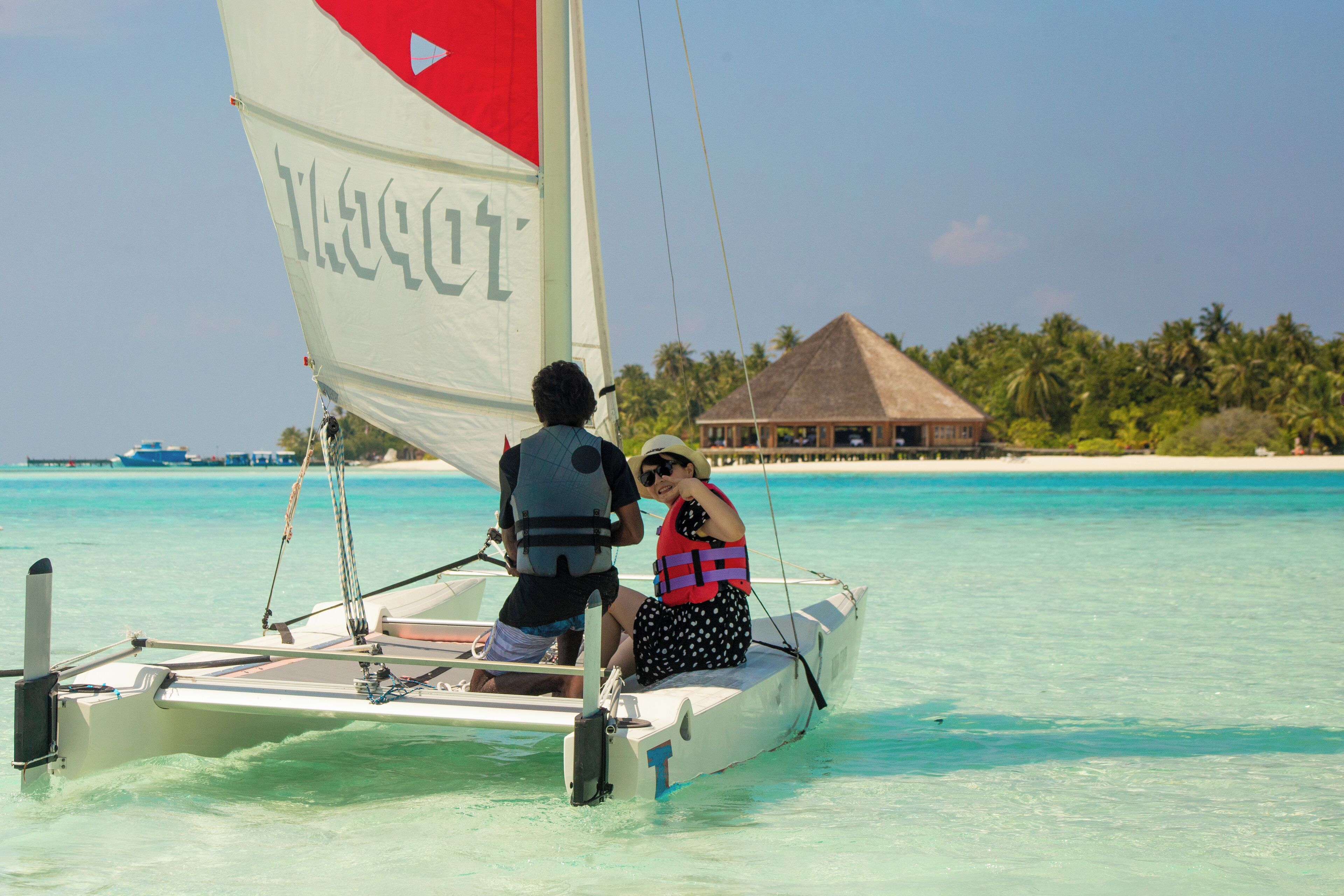 A sailboat with a person steering and another person wearing a life jacket.