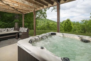 A hot tub under a wooden pergola with a view of a forested hillside.