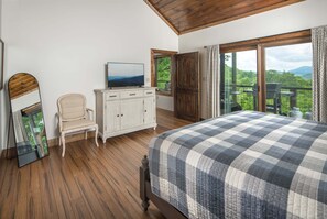 Une chambre avec un grand lit, un téléviseur posé sur un meuble, une chaise et une vue sur l’extérieur grâce à une porte coulissante.