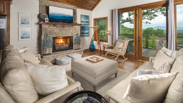 A cozy living room with a fireplace, comfortable seating, and a scenic view through large glass doors. - Upscale Home near Blue Ridge Parkway (Boone)