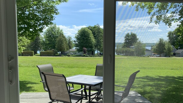 Un patio con mesa y sillas, una terraza de madera y vista a un área verde con árboles y una casa.