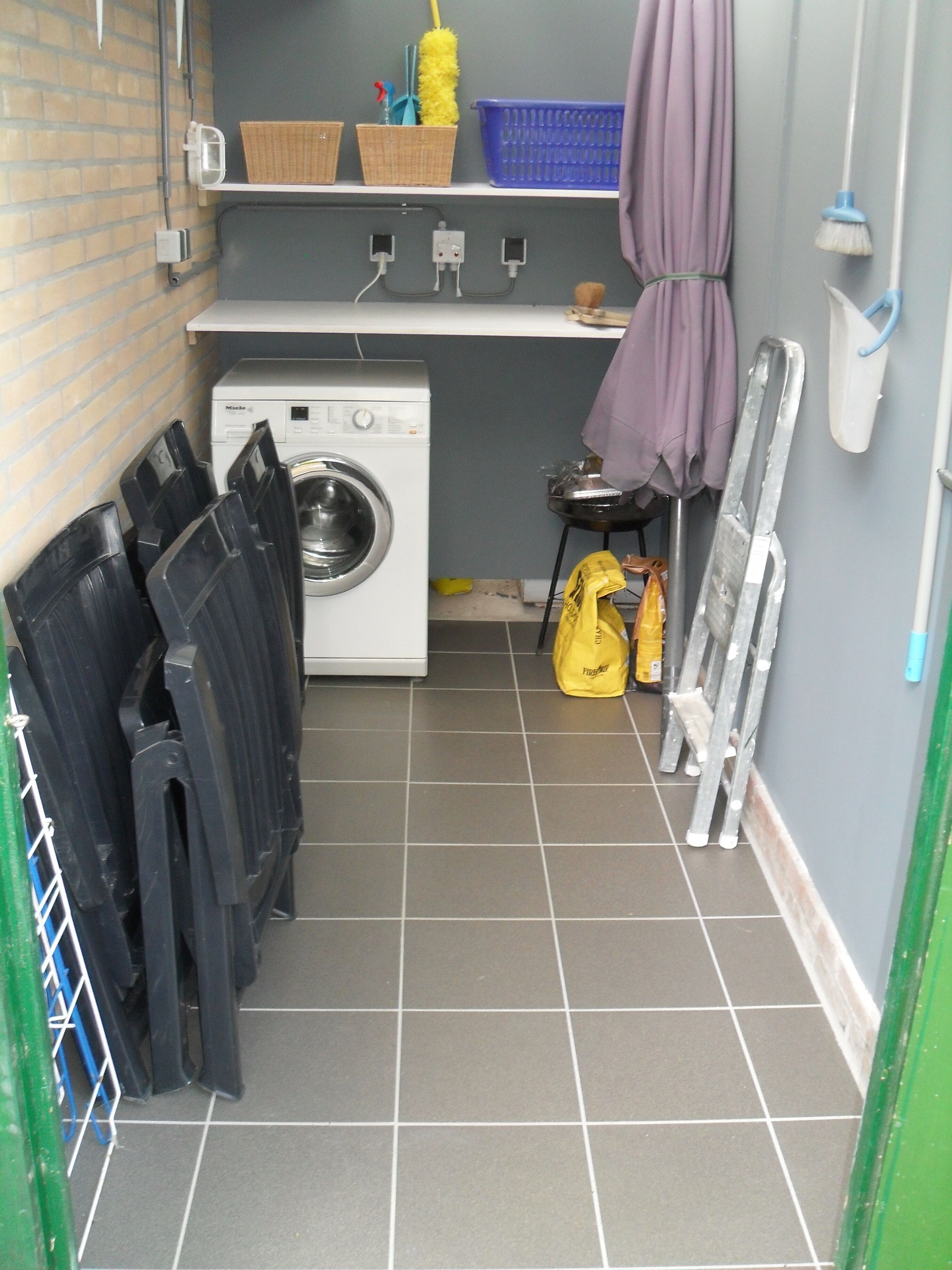 A laundry room with a washing machine, drying racks, a broom, and cleaning supplies.