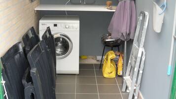 A laundry room with a washing machine, drying racks, a broom, and cleaning supplies.