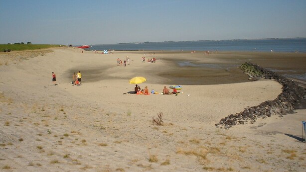 Una playa arenosa con gente, una sombrilla amarilla y una costa rocosa.
