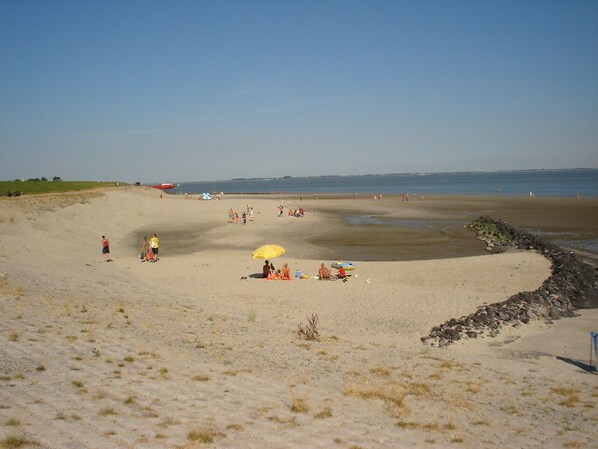 Uma praia arenosa com pessoas, um guarda-sol amarelo e um trecho de costa rochosa.