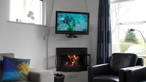 Una sala de estar con chimenea, un televisor montado encima y un sofá con un cojín colorido.