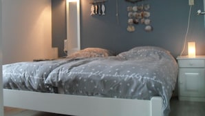 Un dormitorio con cama, mesitas de noche, una estantería en la pared y objetos decorativos.