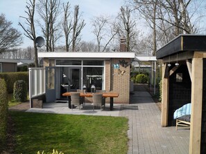 A modern outdoor dining area with a brick wall, glass doors, and a wooden table and chairs.