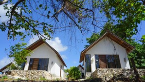 Deux bâtiments blancs aux fondations en pierre, dotés de volets en bois, se dressent sur un fond de ciel bleu azur.