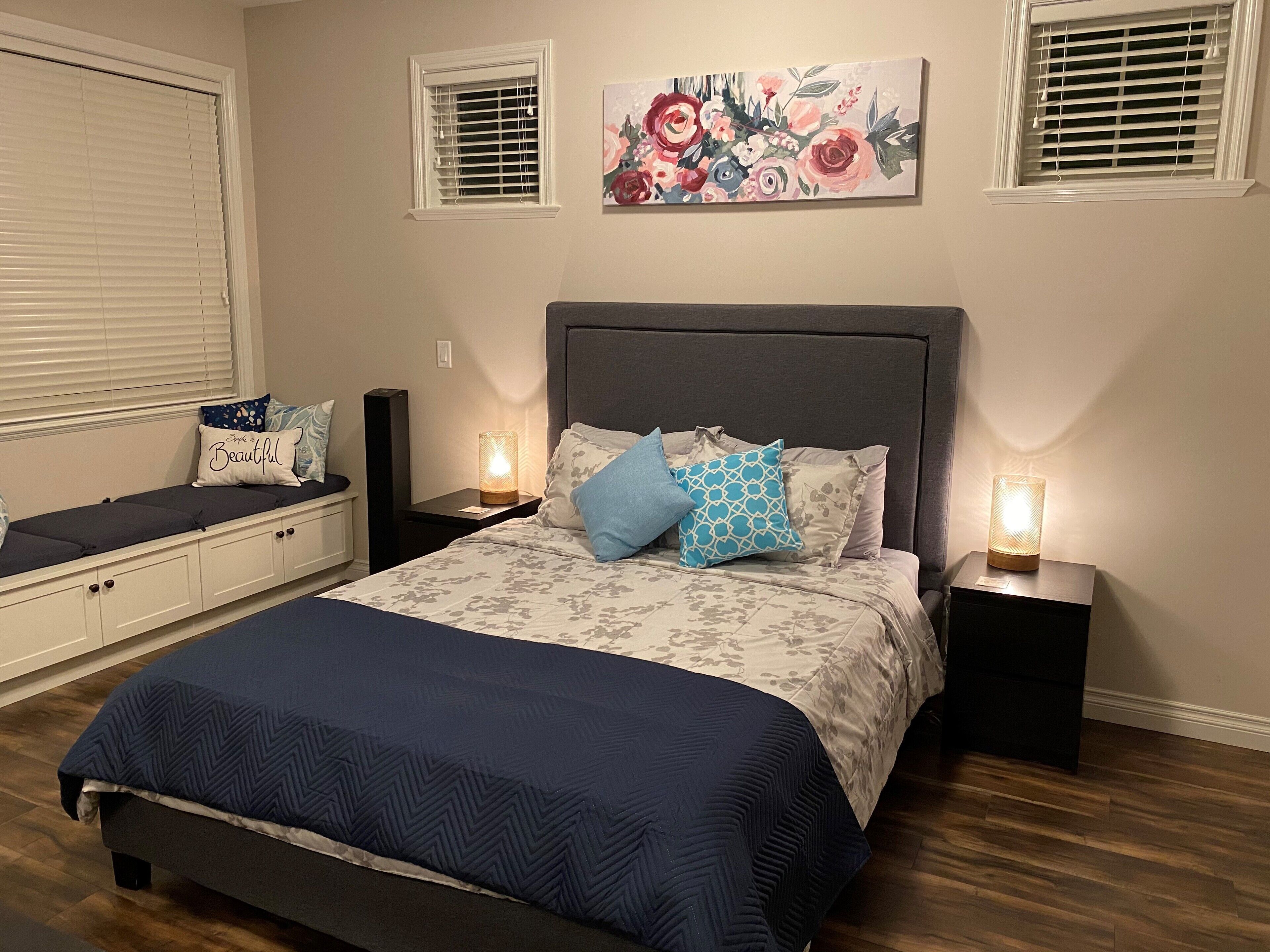 A bedroom with a bed, bedside tables, a bench, and a floral painting on the wall.