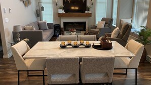 Un salon moderne avec une grande table en marbre, des sièges confortables, une cheminée et un téléviseur.