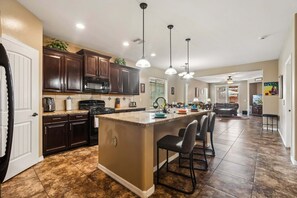 A spacious kitchen with dark wooden cabinets, a central island with bar stools, pendant lighting, and a view to the living area. - MONTHLY SPECIAL Patrick Place Spacious 3 BR Home Golf/Shopping/Gilbert (Gilbert)