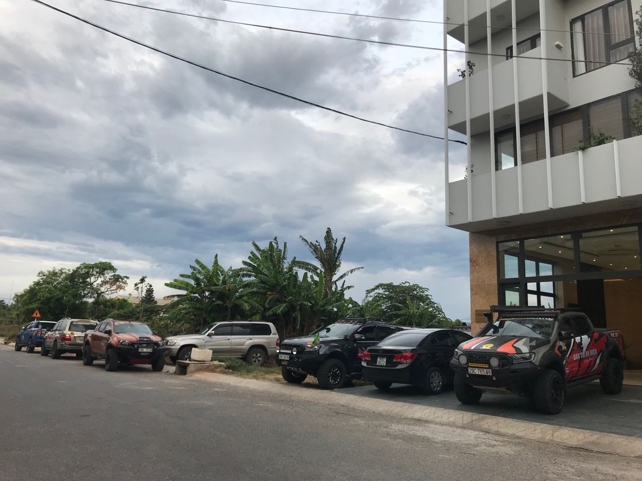 Un aparcament amb diversos vehicles, incloent-hi una pickup negra amb un disseny vermell i blanc, estacionats davant d'un edifici amb grans finestres i un balcó.