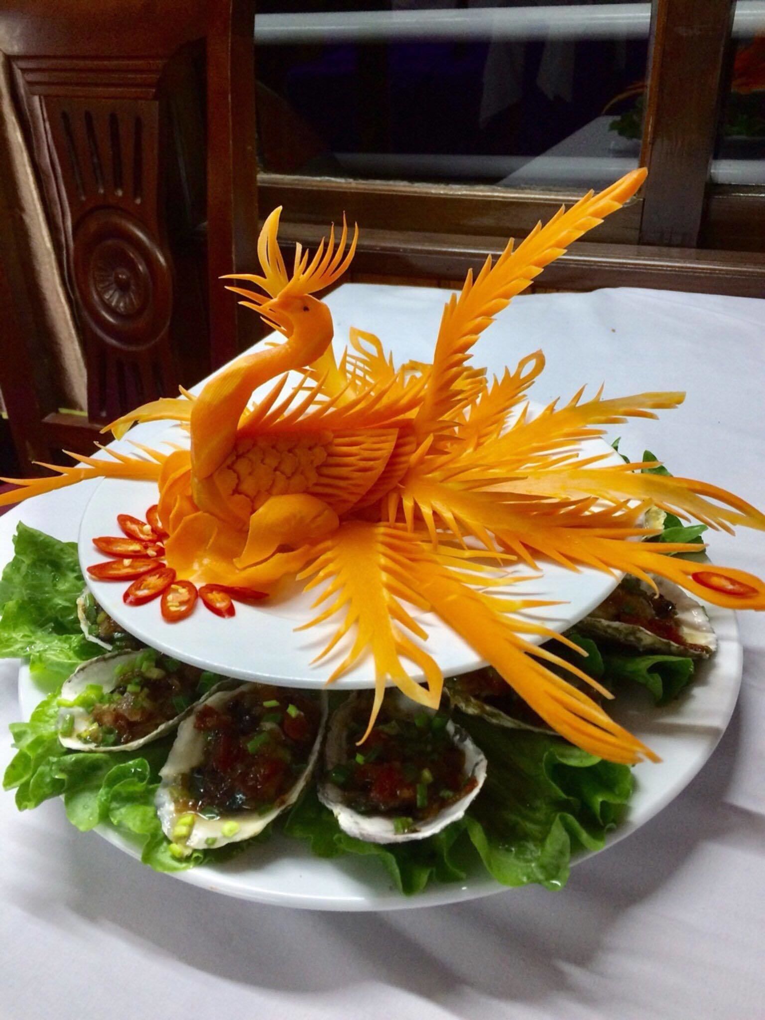 Un plato con un pájaro naranja tallado y hojas, rodeado de lechuga y ostras.