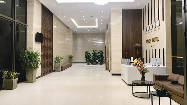 A modern hotel lobby with a reception desk, seating area, and potted plants.