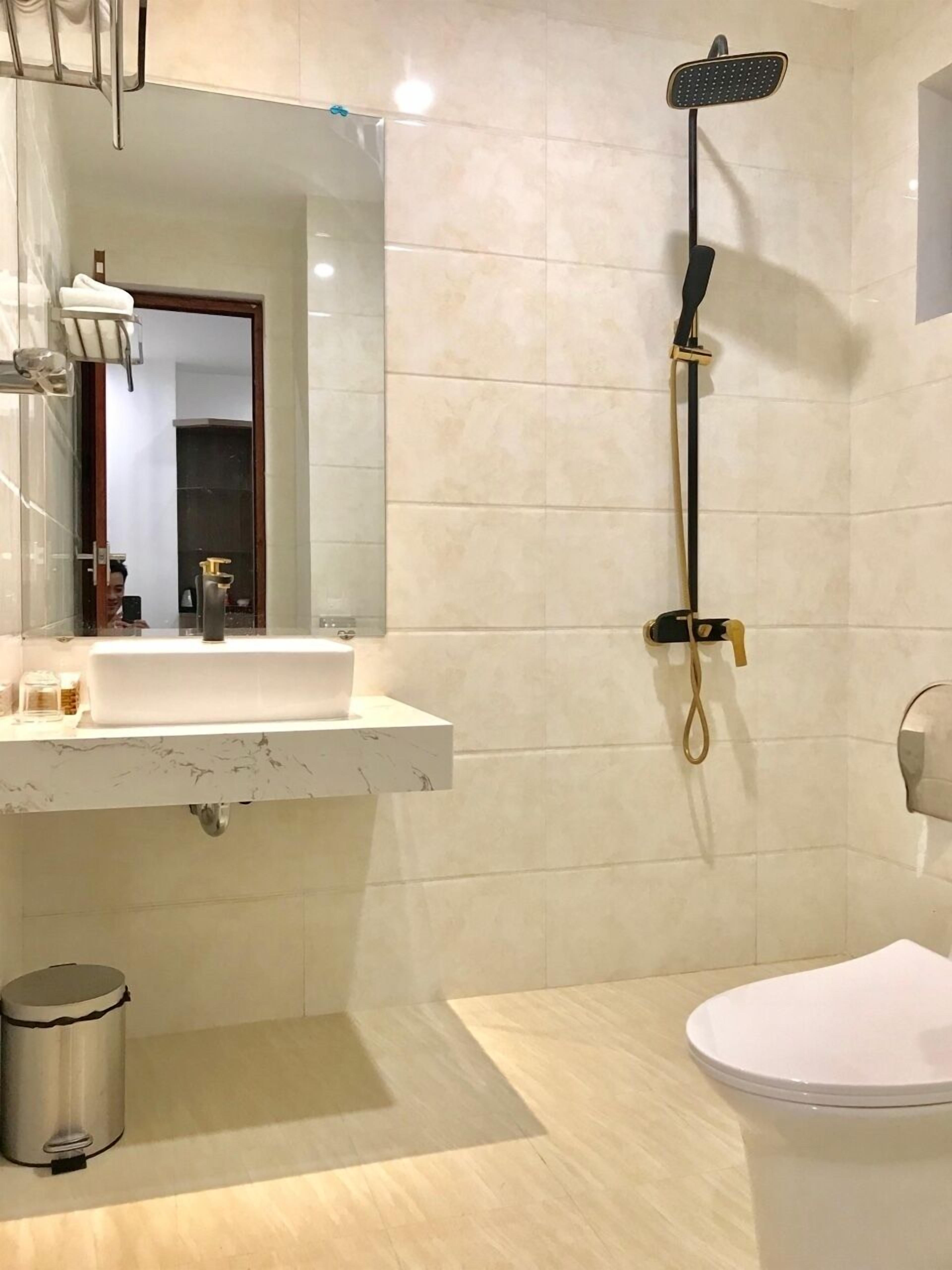 Un baño con lavamanos, espejo, ducha, inodoro y cubo de basura.