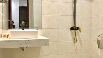 Un baño con lavamanos, espejo, ducha, inodoro y cubo de basura.