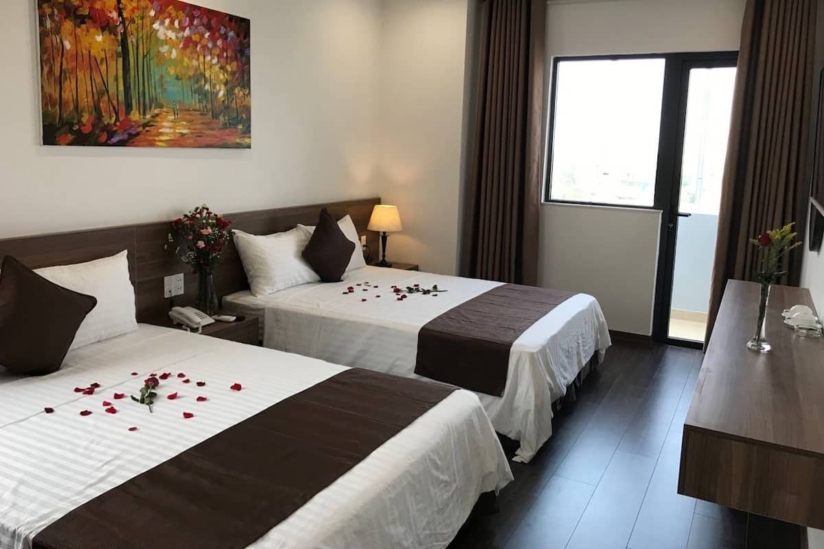 Quarto de hotel com duas camas, um quadro na parede, uma escrivaninha com um vaso e uma janela com cortinas.