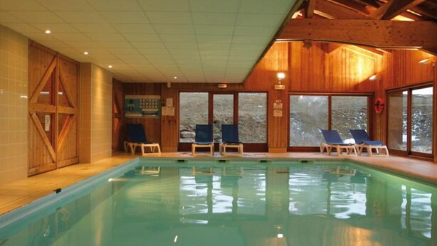 Une piscine intérieure aux murs et au plafond en bois, entourée de chaises longues.