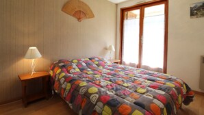 A bedroom with a bed, two bedside tables, a lamp, a fan, and a window with curtains. - Apartment for 6 in Val Cenis Lanslevillard, includes parking (Lanslevillard)