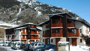 A hotel with multiple balconies, a parking lot with several cars, and a sign indicating camping facilities. - Apartment for 6 in Val Cenis Lanslevillard, includes parking (Lanslevillard)