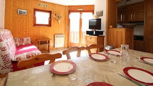 A dining area with wooden walls, a television, and a kitchen in the background. - Apartment for 6 in Val Cenis Lanslevillard, includes parking (Lanslevillard)