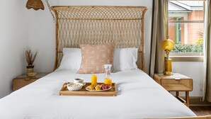 Una cama bien hecha con una bandeja de desayuno, un cabecero de mimbre y vistas al exterior con vegetación.