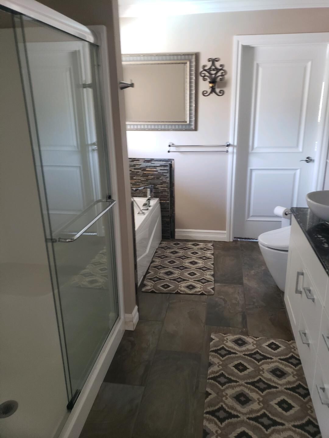 A bathroom with a glass shower enclosure, a bathtub, a toilet, and a sink.
