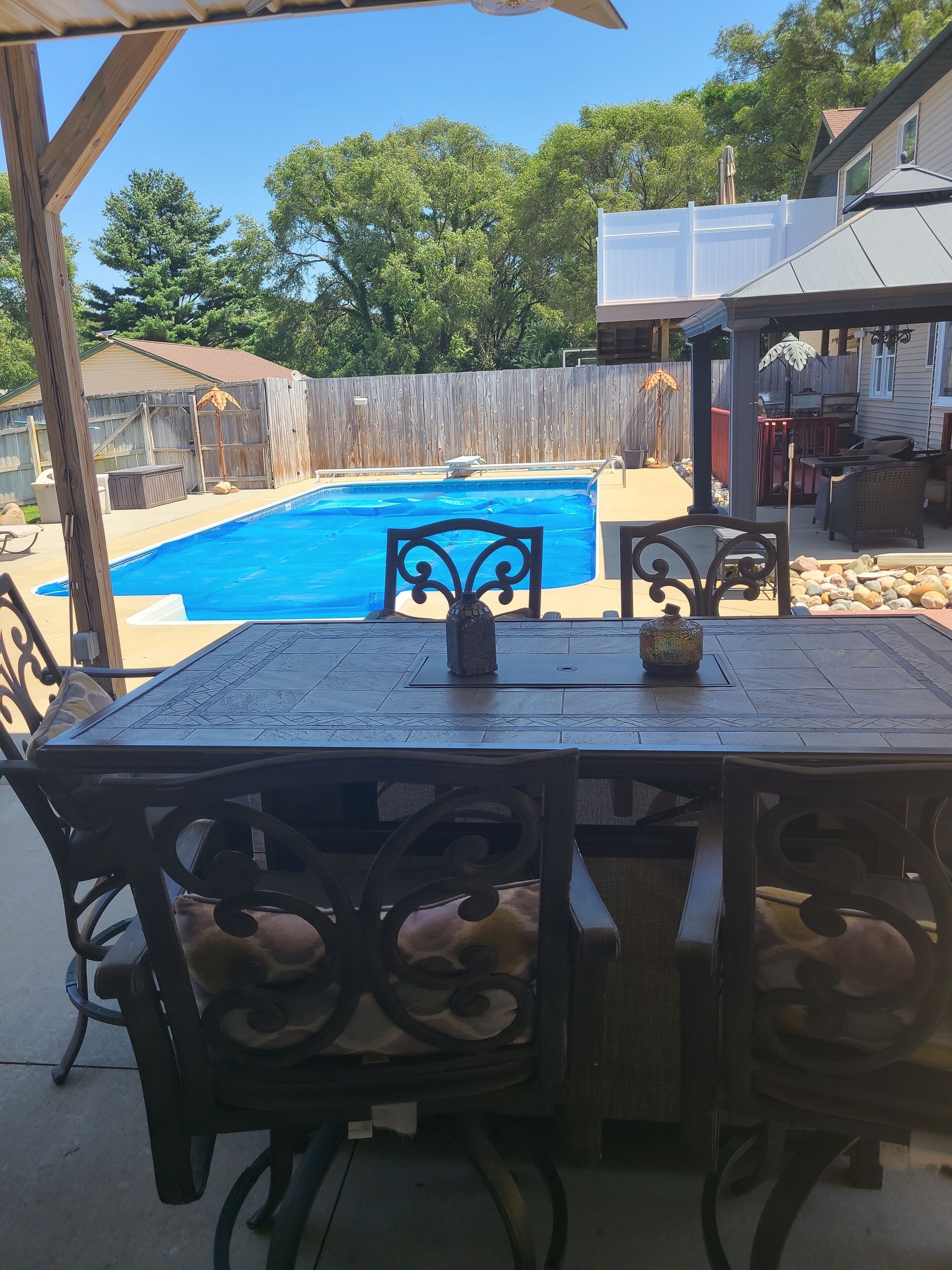 Ein Garten mit Schwimmbecken, Terrassenmöbeln und einer überdachten Sitzgelegenheit.