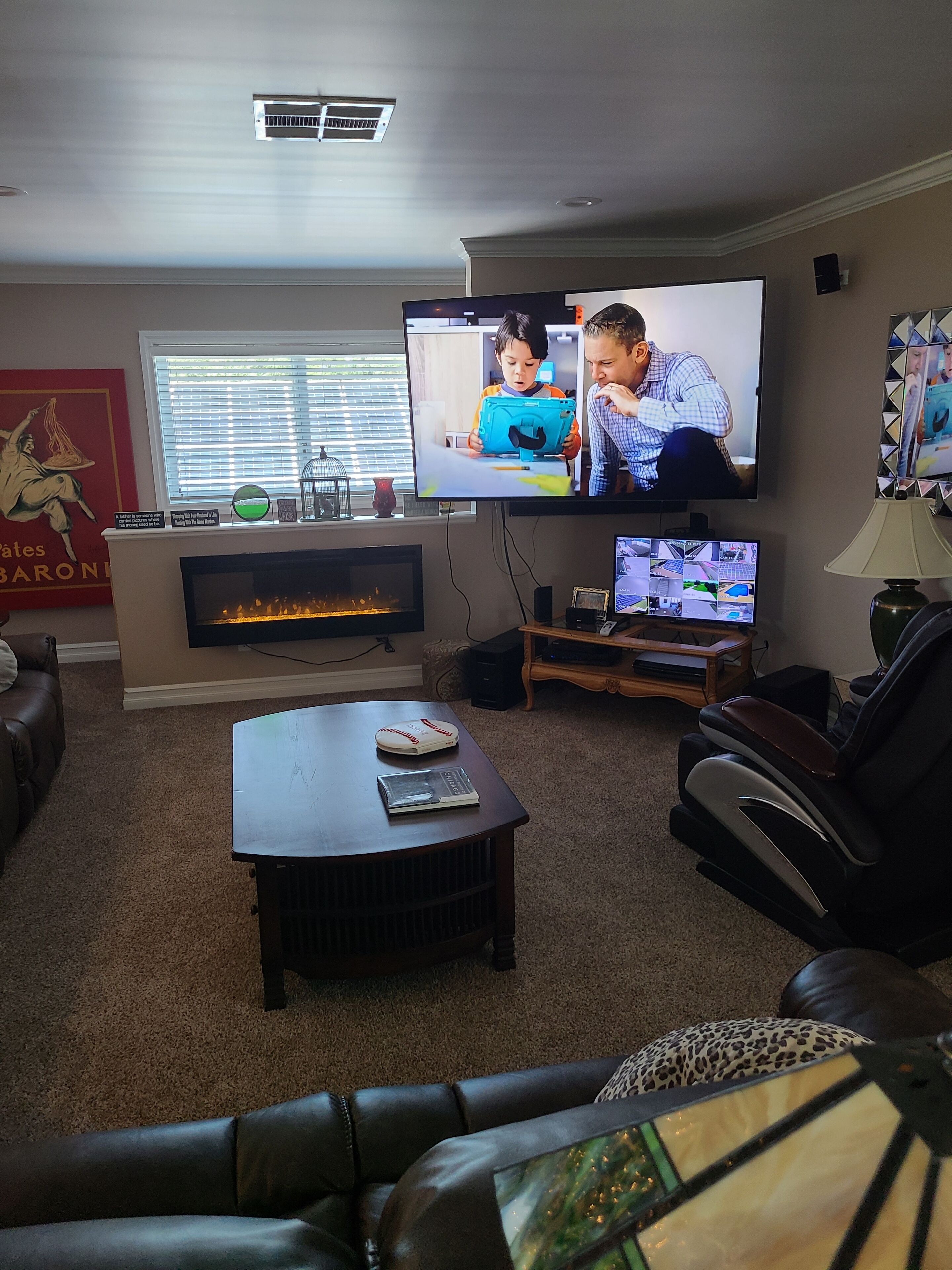 A living room with a fireplace, a large flat-screen TV mounted on the wall, a leather sofa, and a massage chair.